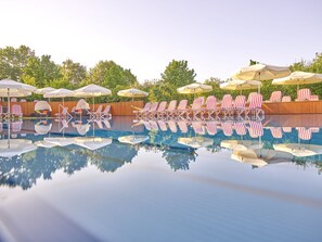 A swimming pool with striped lounge chairs and umbrellas, surrounded by a wooden deck and trees. - Parkhotel Bad Griesbach (Bad Griesbach im Rottal)