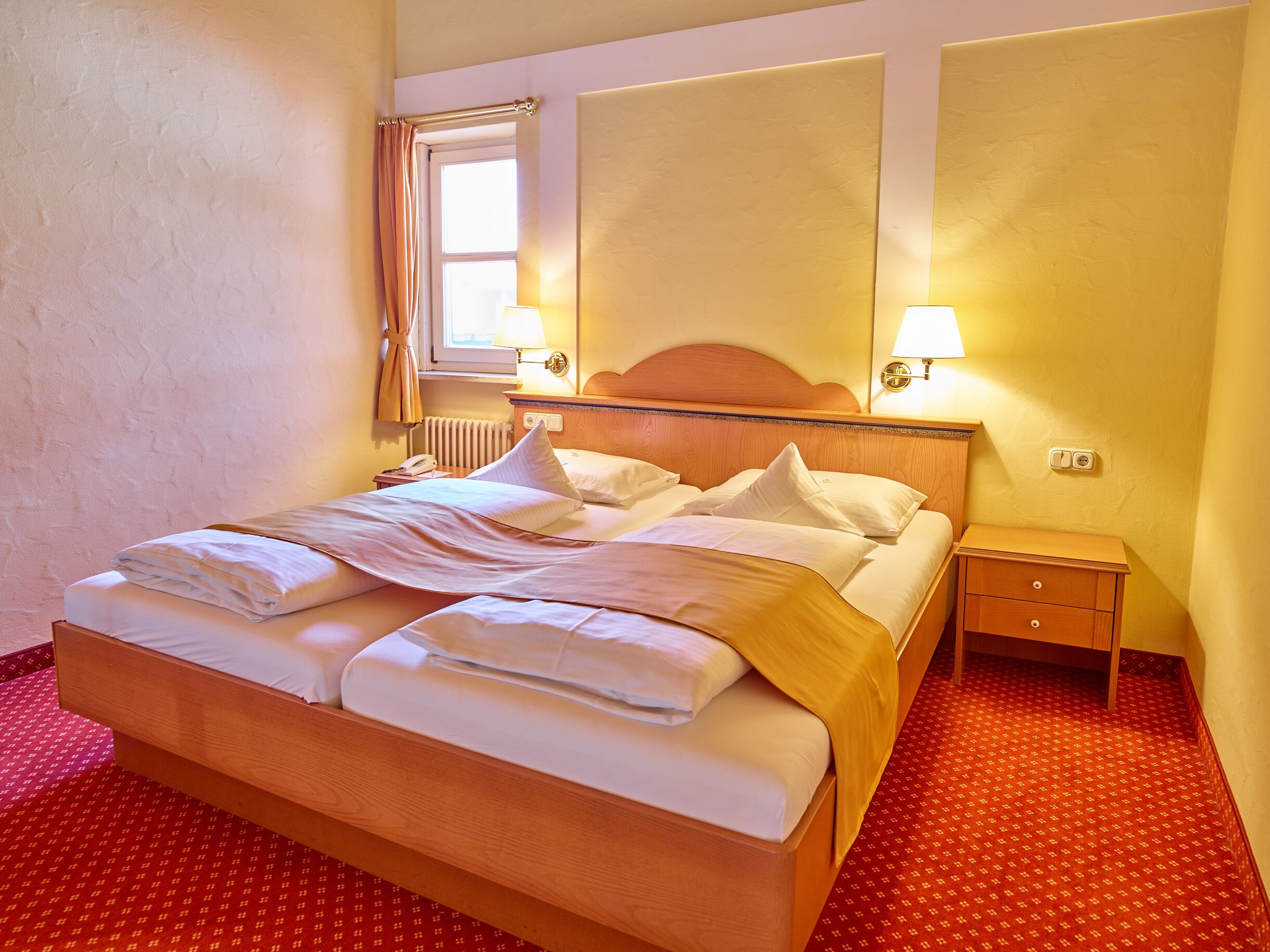 Une chambre d’hôtel avec un grand lit, une table de chevet, une lampe et une fenêtre avec des rideaux.