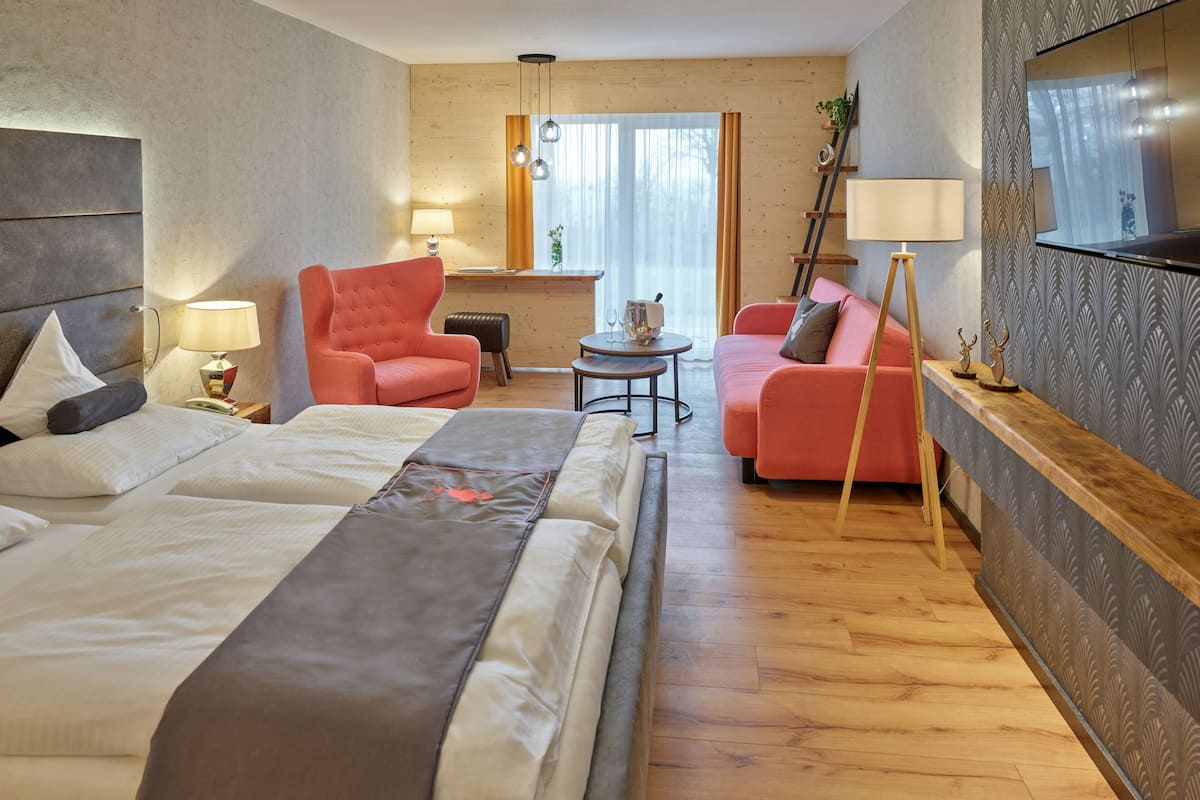 A modern hotel room with a large bed, a sofa, a chair, a small table, and a mirror.
