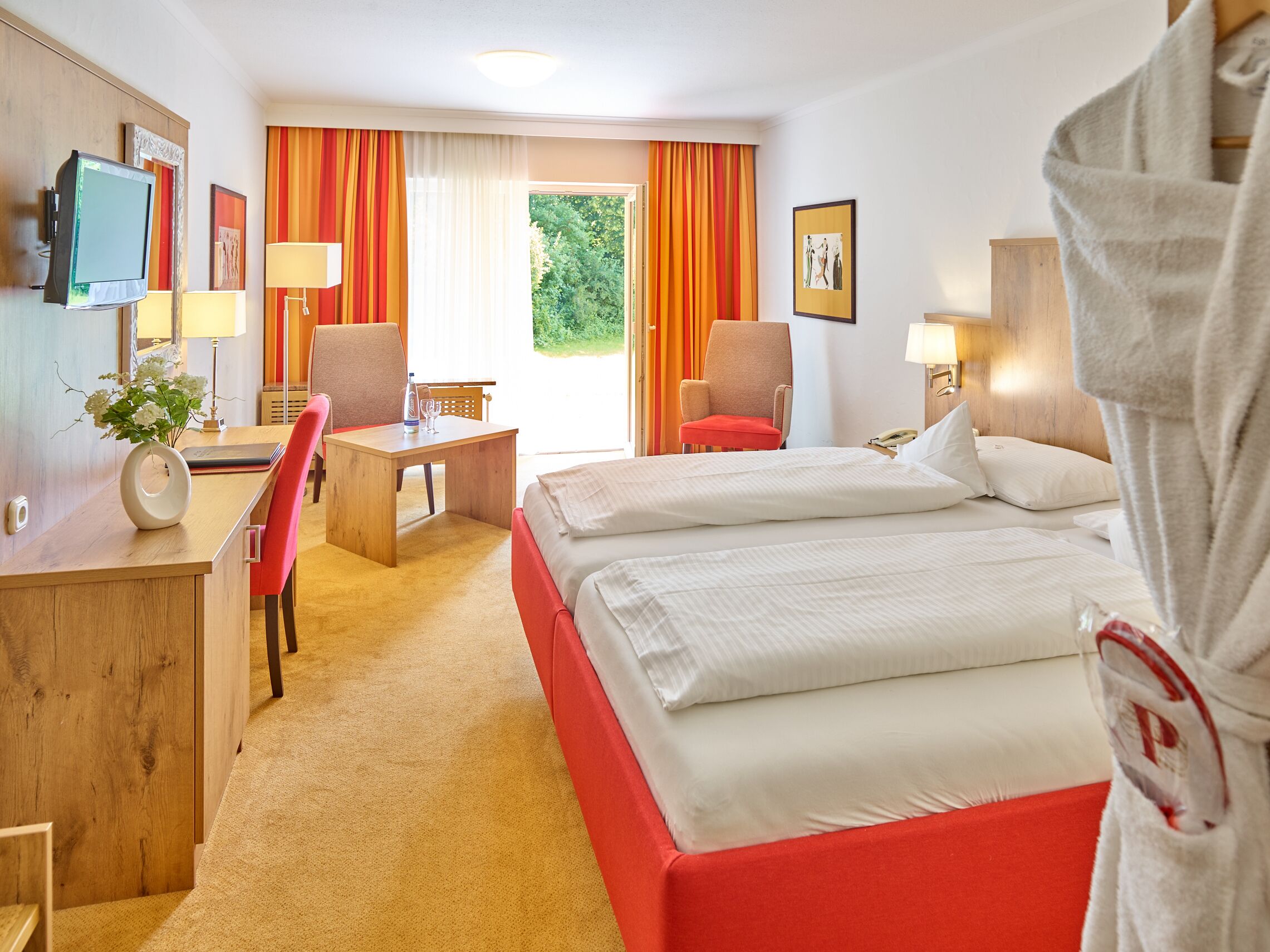 A hotel room with a bed, a desk, a chair, a TV, and a window with curtains.