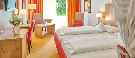 A hotel room with a bed, a desk, a chair, a TV, and a window with curtains.