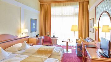 Une chambre d’hôtel équipée d’un lit, d’un bureau, d’une chaise, d’une télévision et d’une fenêtre avec des rideaux.