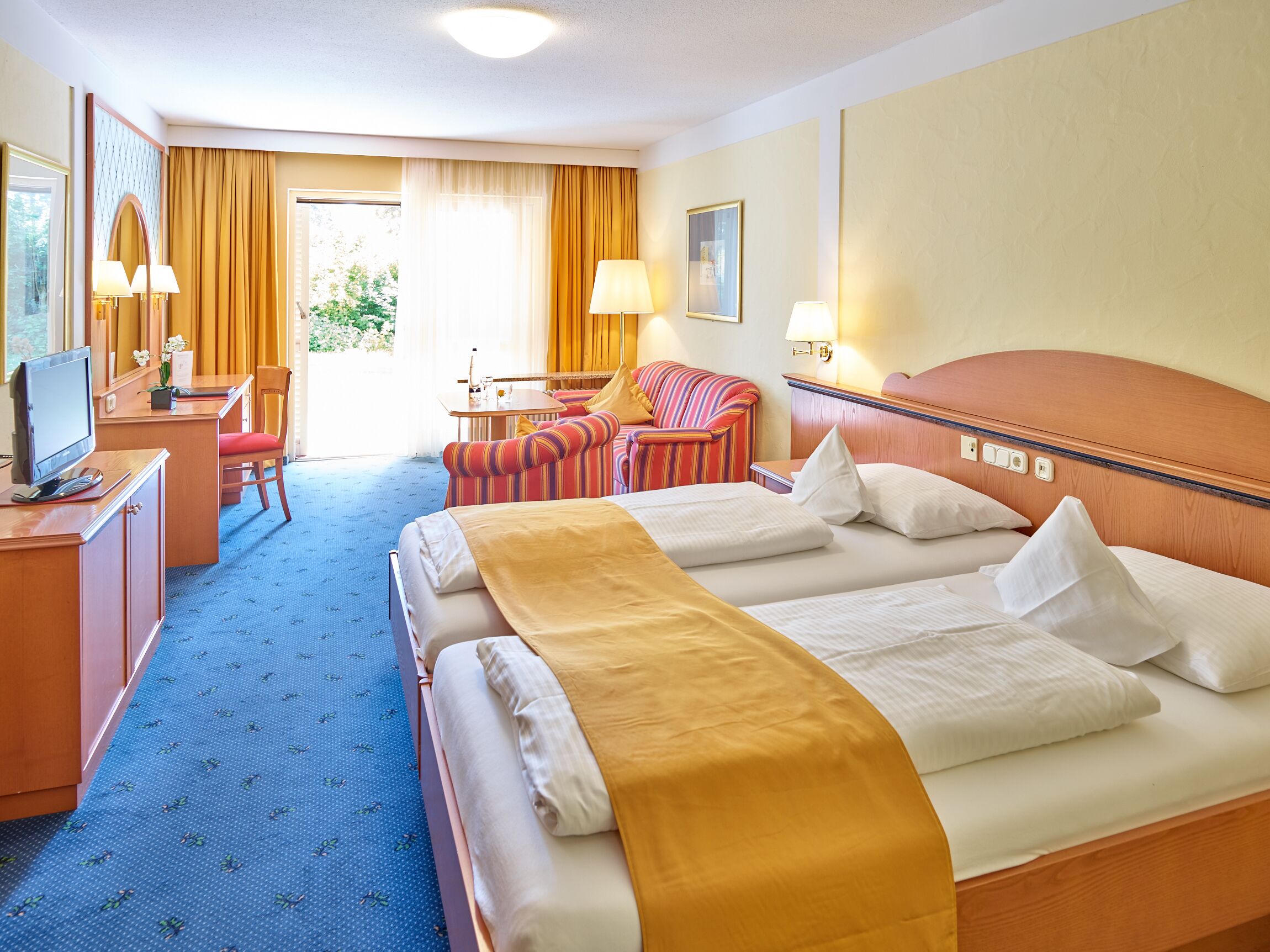 A hotel room with a large bed, a desk with a computer, a chair, and a small table.