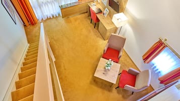 A hotel room with a wooden desk, a red chair, a small table with a vase, and a staircase.
