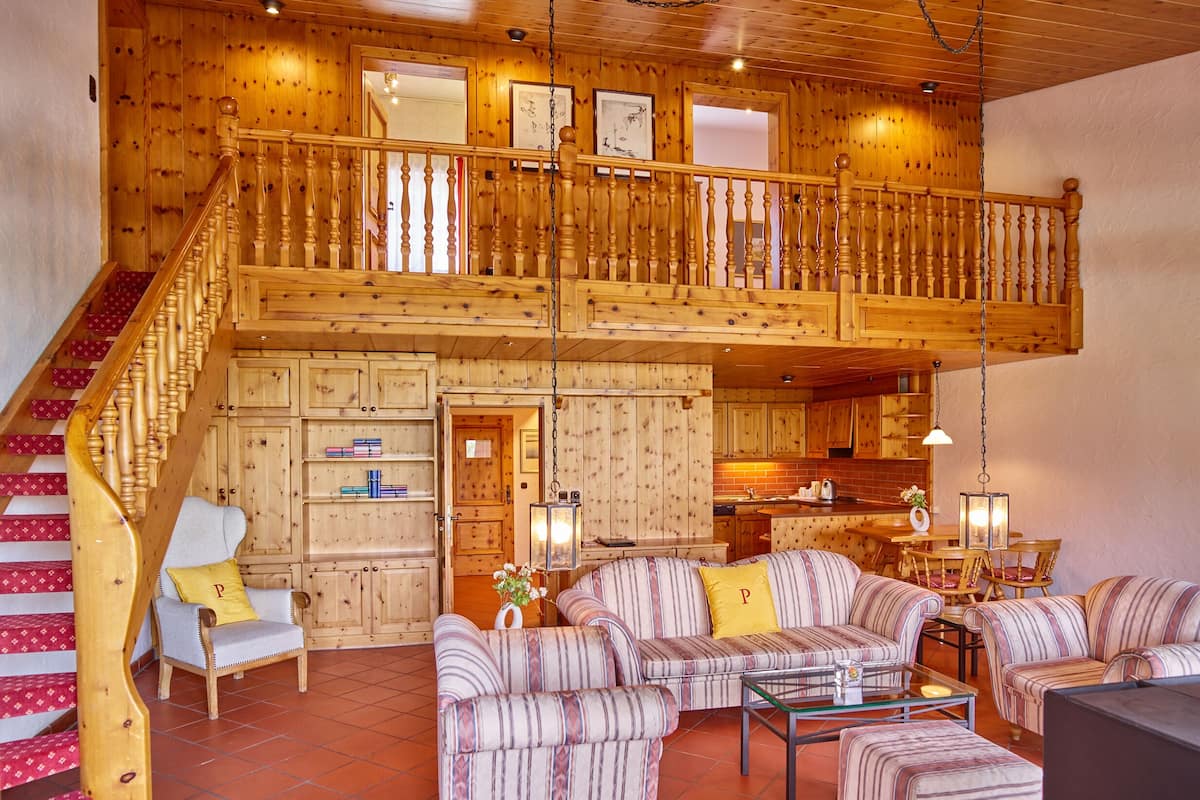 A wooden cabin with a staircase, a living room with striped sofas, a dining area, and a kitchen.