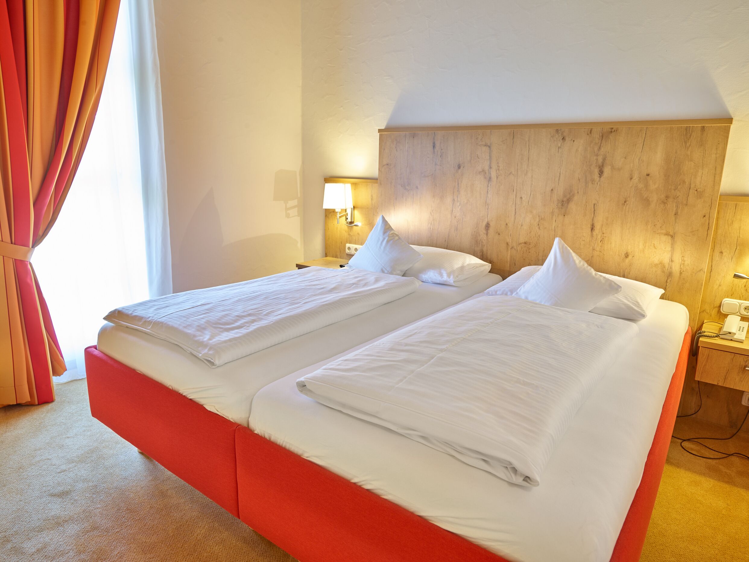 A double bed with white linens, a wooden headboard, bedside lamps, and a telephone on a wooden nightstand.