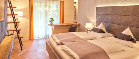 A modern hotel room with a large bed, wooden floor, a desk with a chair, a ladder, and a window with curtains.