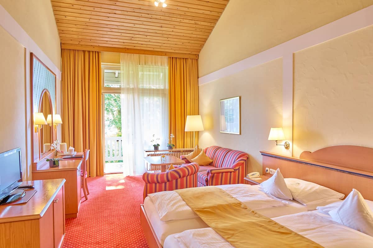 A hotel room with a bed, a desk, a chair, a sofa, and a small table.
