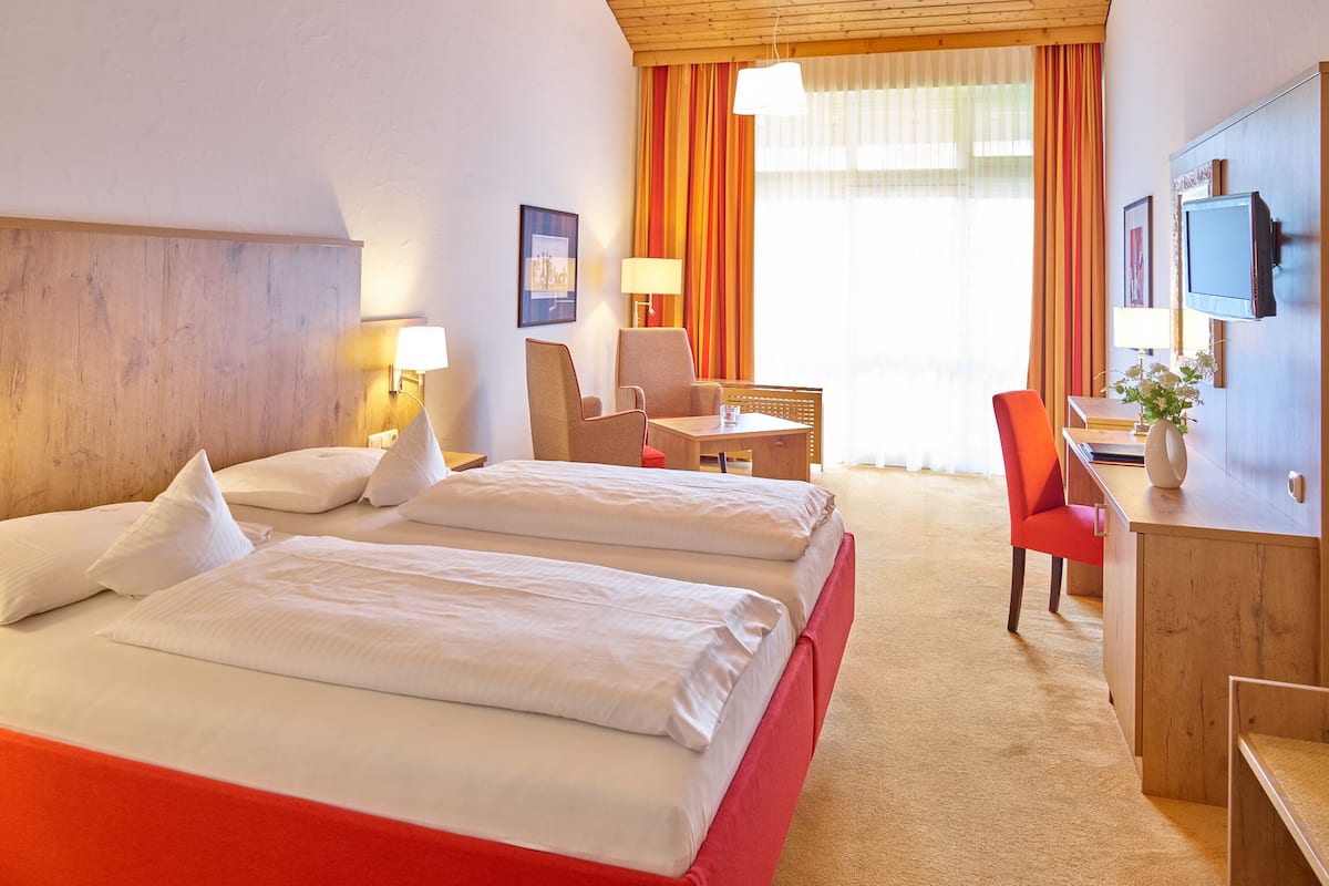 A hotel room with two beds, a desk, a chair, a TV, and a window with curtains.