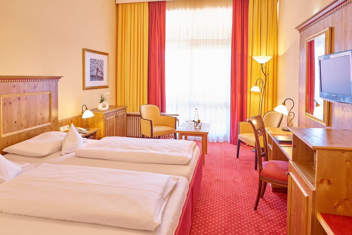 A hotel room with two beds, a desk with a chair, a TV, and a window with curtains.