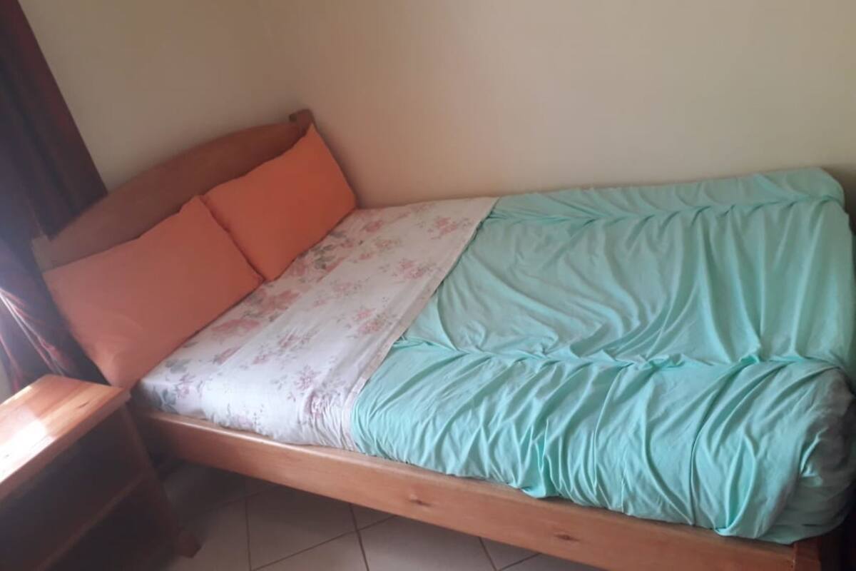 A single bed with a wooden frame, a floral-patterned bedspread, and two orange pillows.