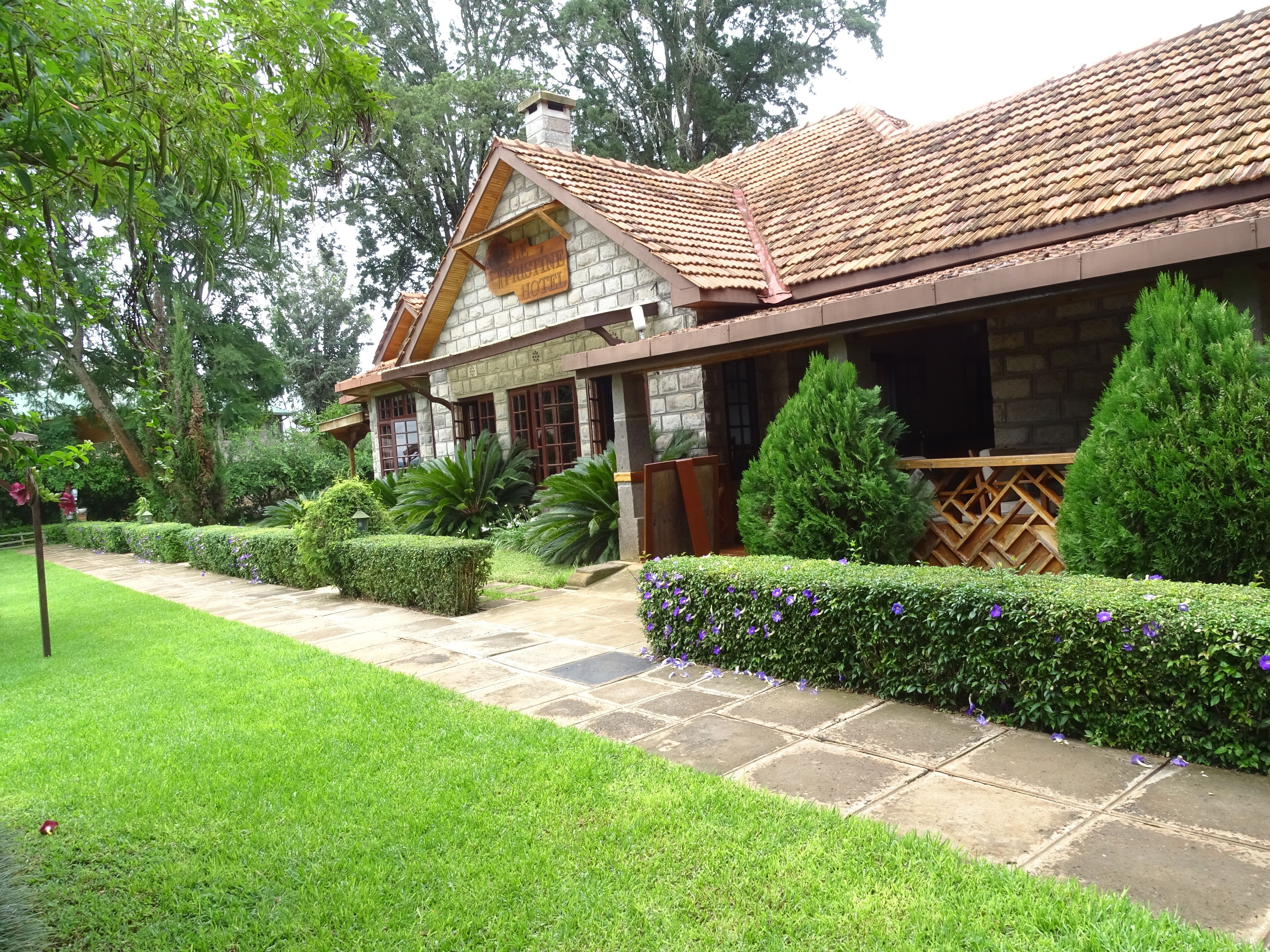 A stone building with a tiled roof, surrounded by well-maintained hedges and a stone pathway.