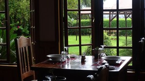 Un coin repas avec une table dressée pour deux personnes, de grandes fenêtres donnant sur un jardin.