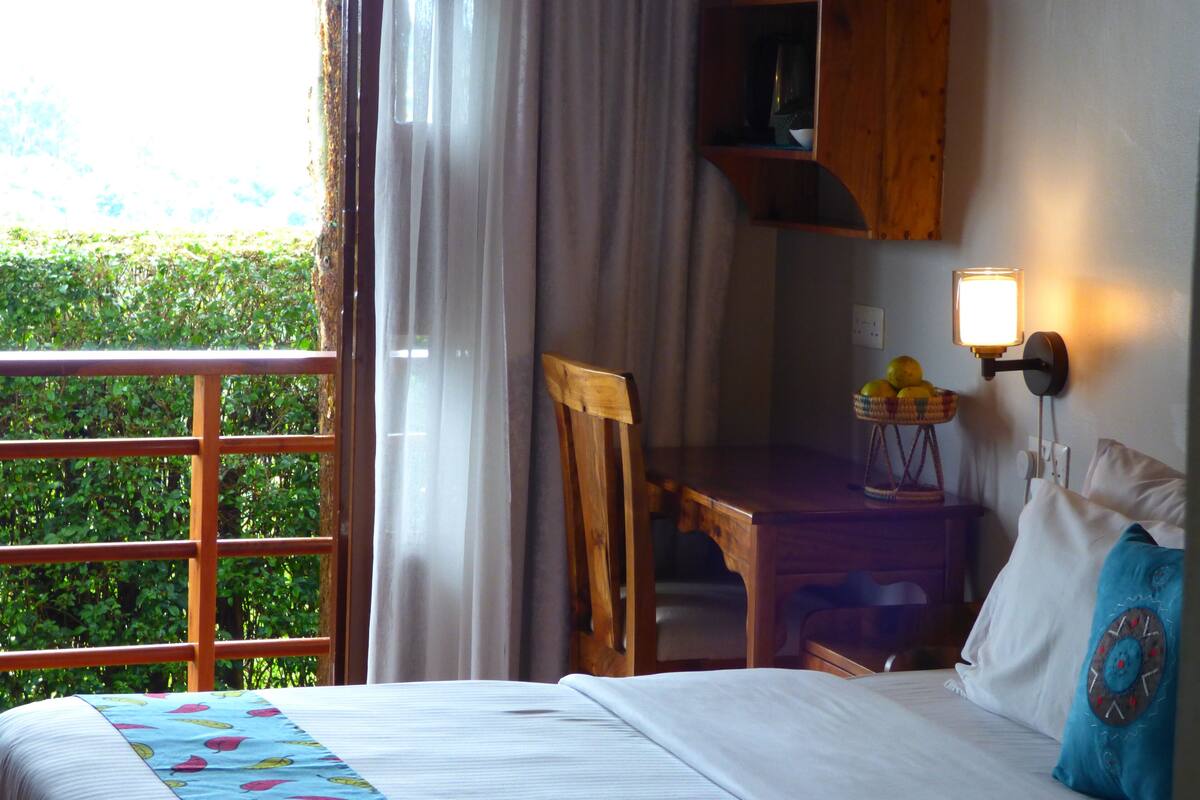 A bedroom with a bed, a wooden chair, a small table with fruit, and a wall-mounted lamp.
