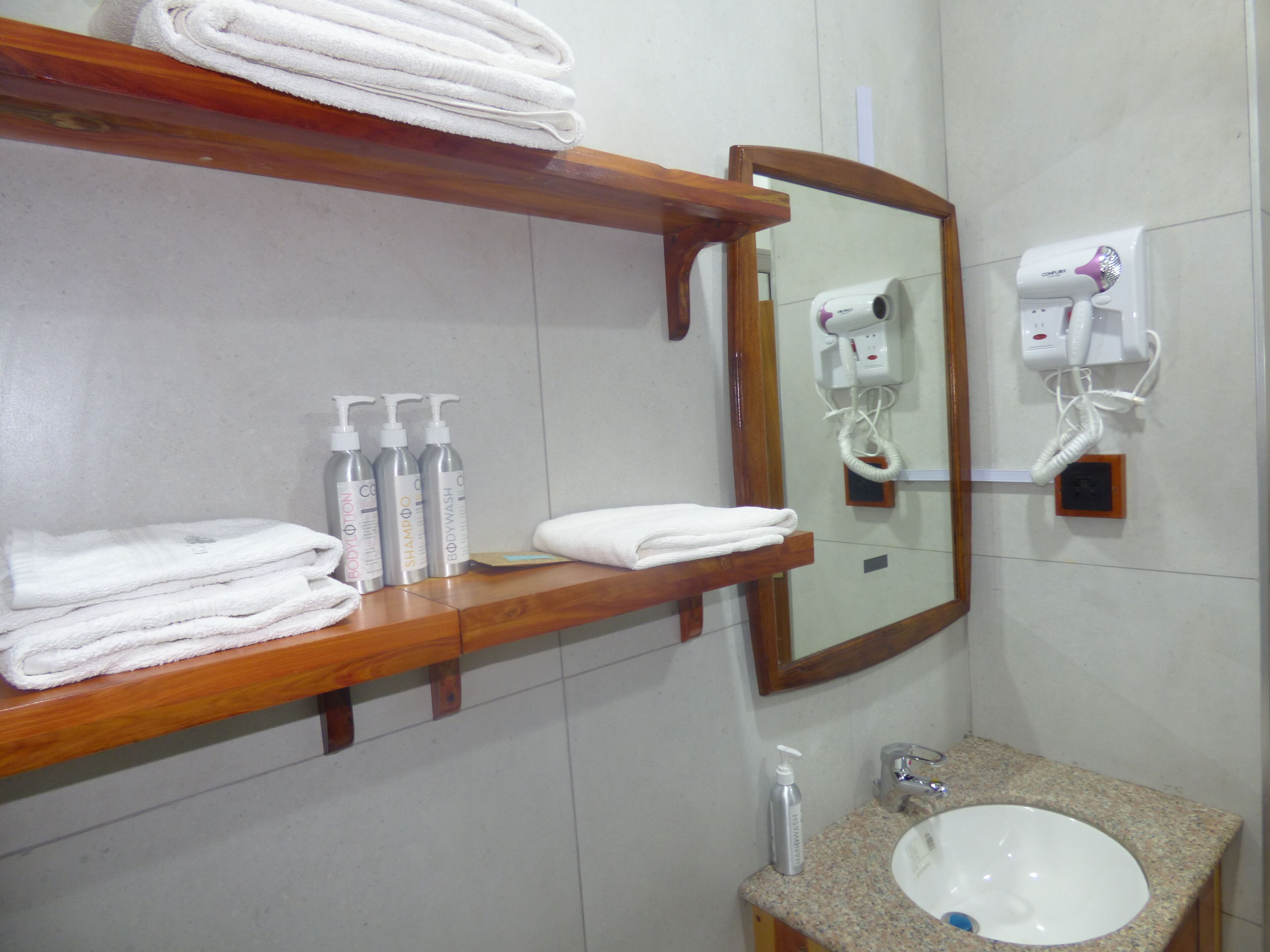 Un baño con un estante de madera que sostiene toallas, un lavabo y un espejo. Hay botellas de champú y gel de baño en el estante.