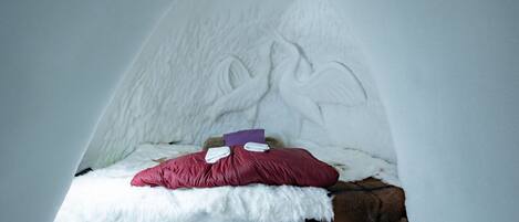 A cozy room with a bed featuring a white, fluffy bedspread and a red pillow.