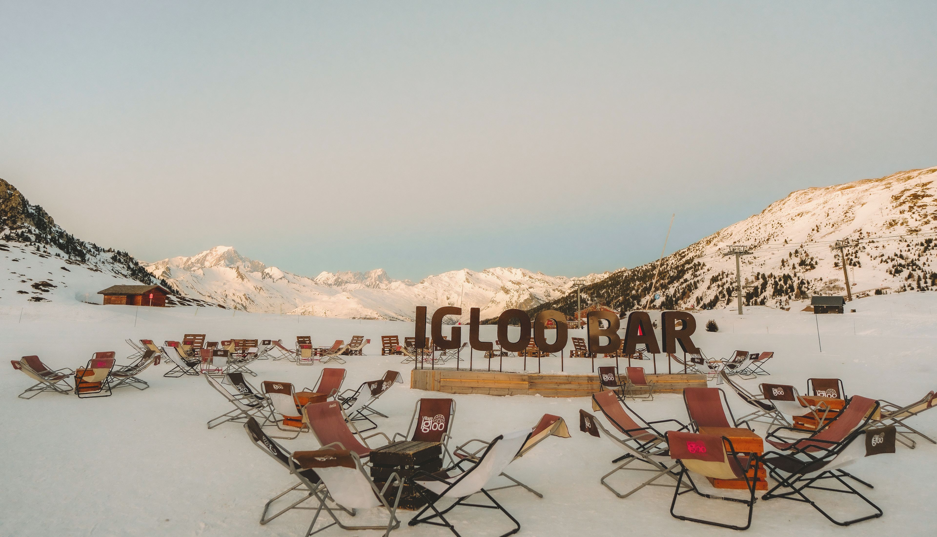 A snow-covered landscape with a bar named 'IGLOO BAR' and multiple lounge chairs arranged for seating.
