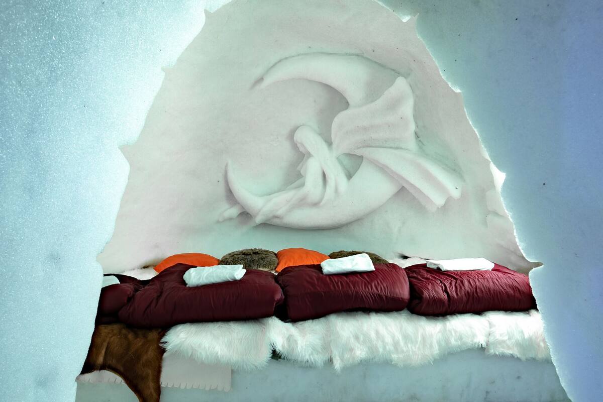 A bed with a white furry blanket and multiple pillows in various colors.