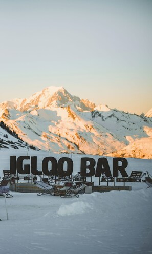 Paisatge de muntanya nevada amb un bar anomenat 'IGLOO BAR' en primer pla.