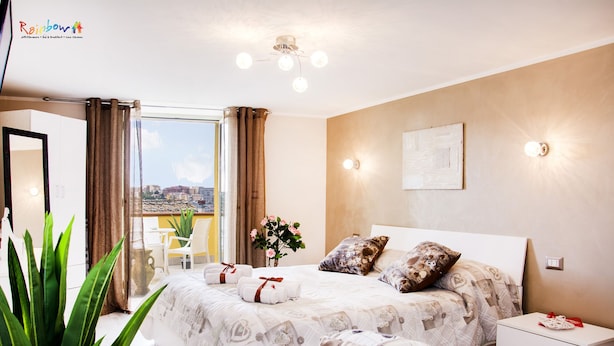 A hotel room with a large bed, a bedside table, a nightstand, a potted plant, and a view of the city. - B&B Porta San Paolo (Campobasso)