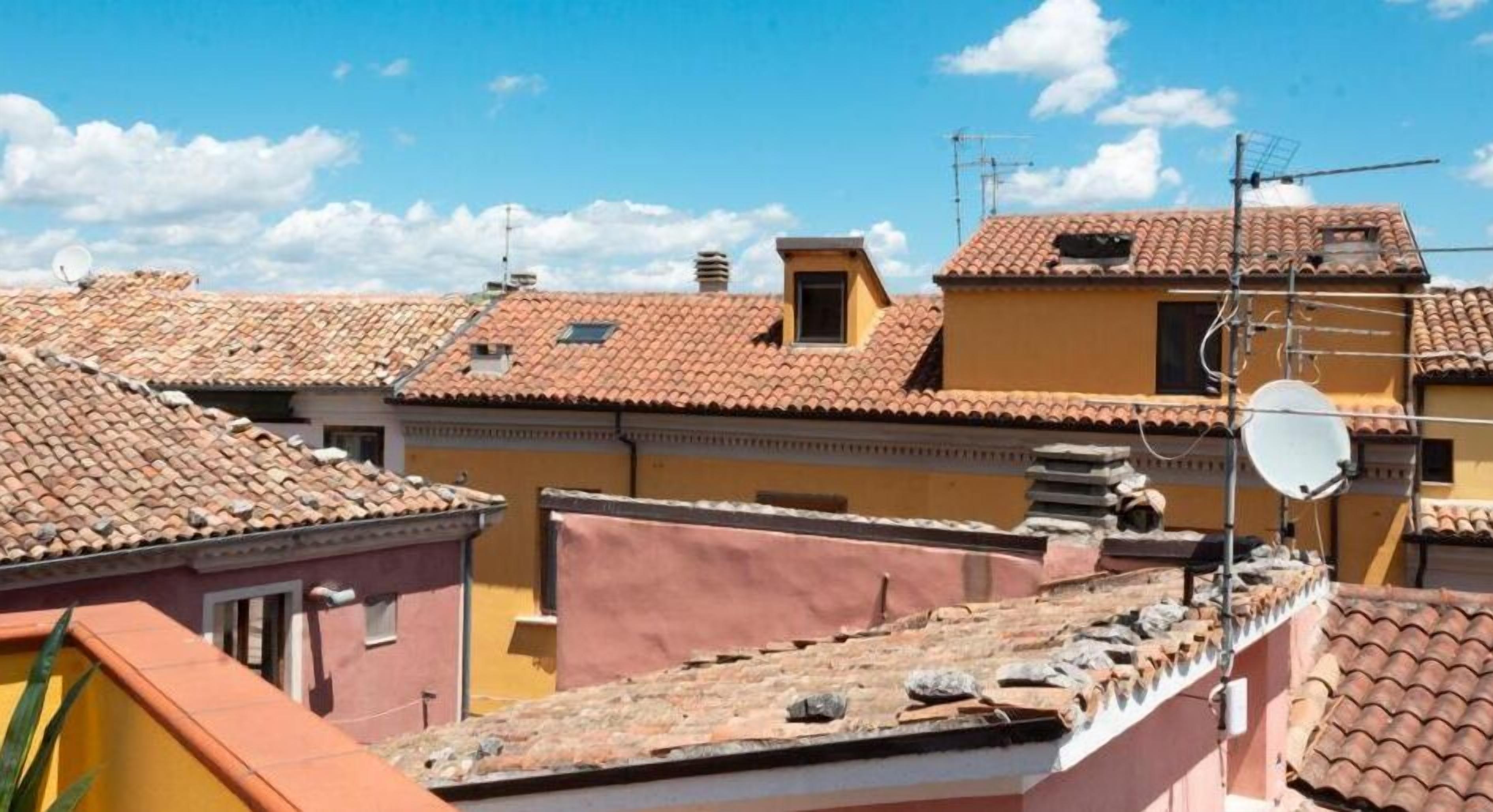 Un quartier résidentiel avec des toits recouverts de tuiles en terre cuite, des antennes paraboliques et un ciel d’un bleu éclatant.