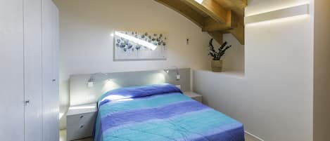 A bedroom with a bed, nightstands, a wall-mounted light, a ceiling skylight, and a potted plant.