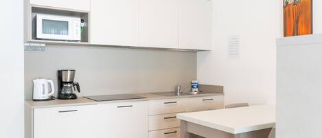 A modern kitchen with white cabinets, a microwave, a coffee maker, and a sink.