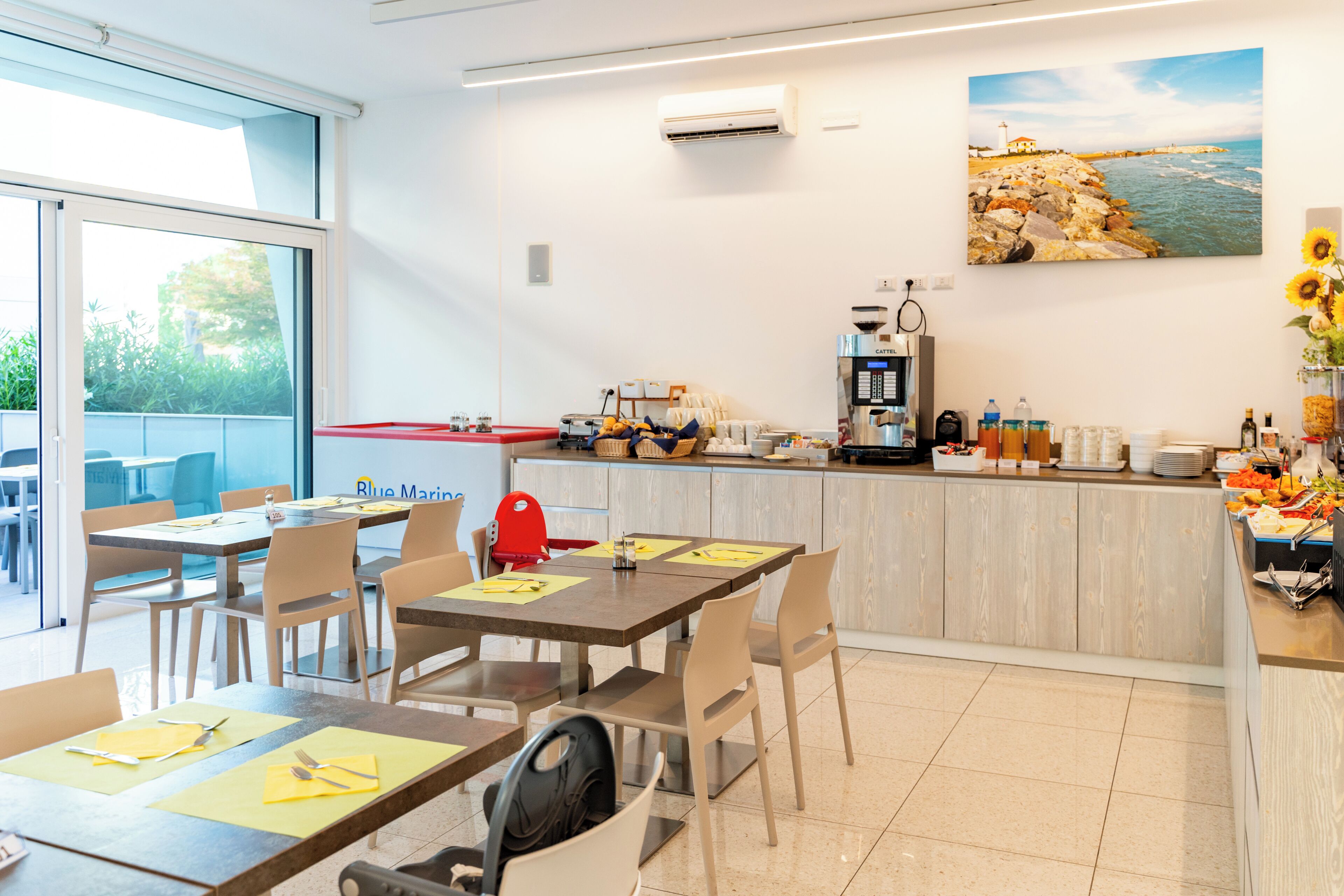 A modern dining area with tables, chairs, a coffee station, and a view of the outdoors.