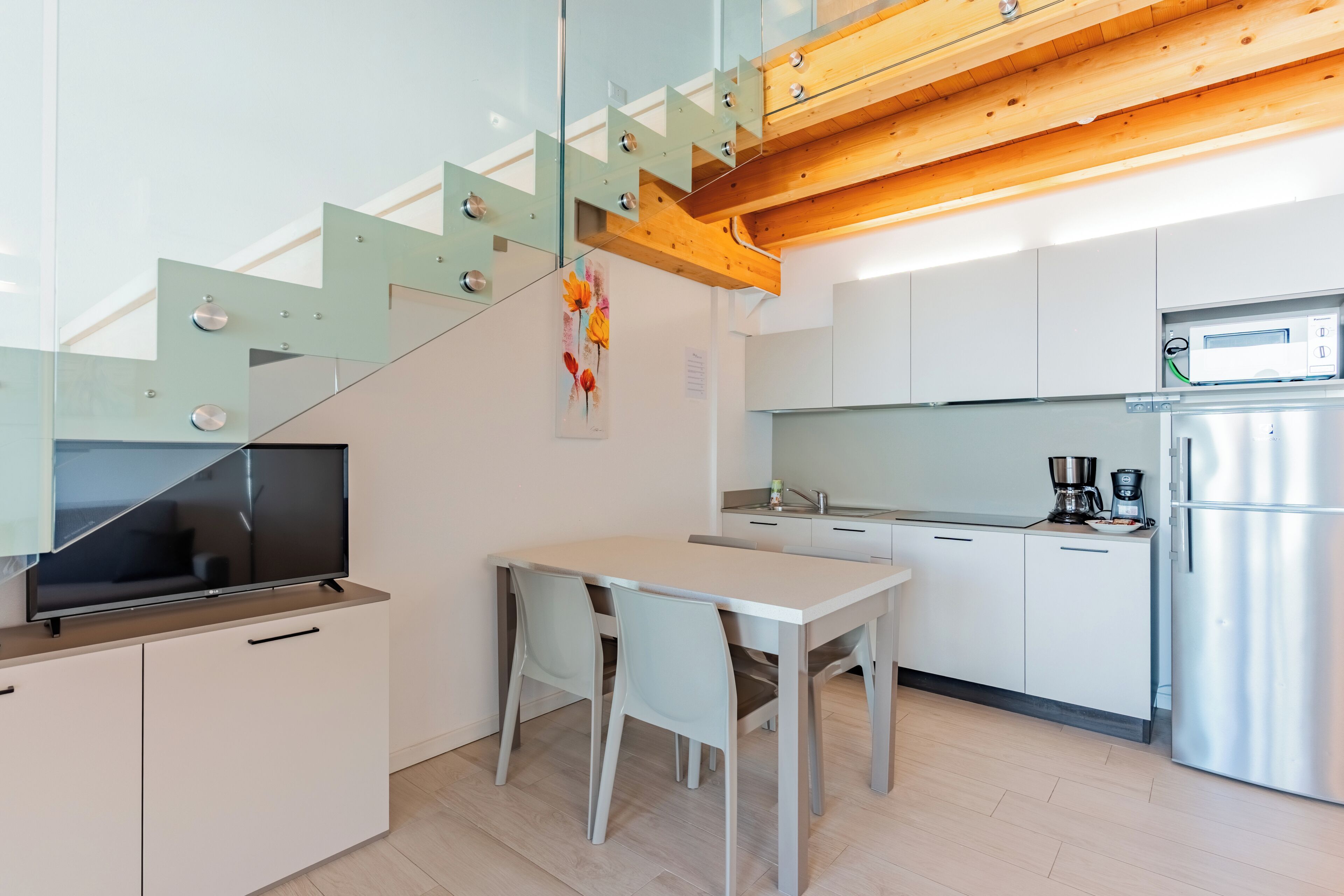 Une cuisine moderne avec un coin repas, un four encastré et un escalier doté de rampes en verre.