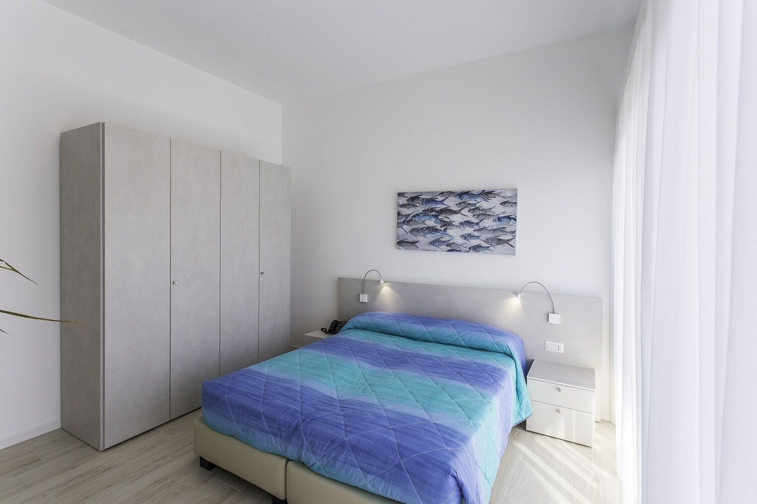 A bedroom with a bed, a wardrobe, a nightstand, and a wall-mounted artwork.