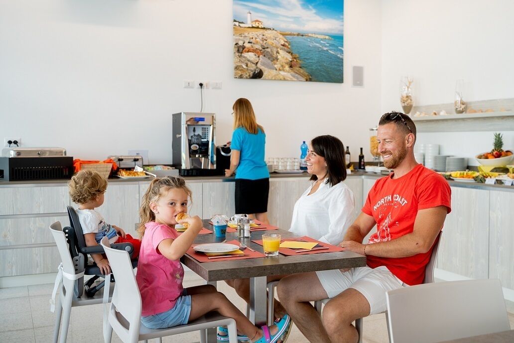 Eine Familie isst an einem Tisch, im Hintergrund ist eine Küche zu sehen.