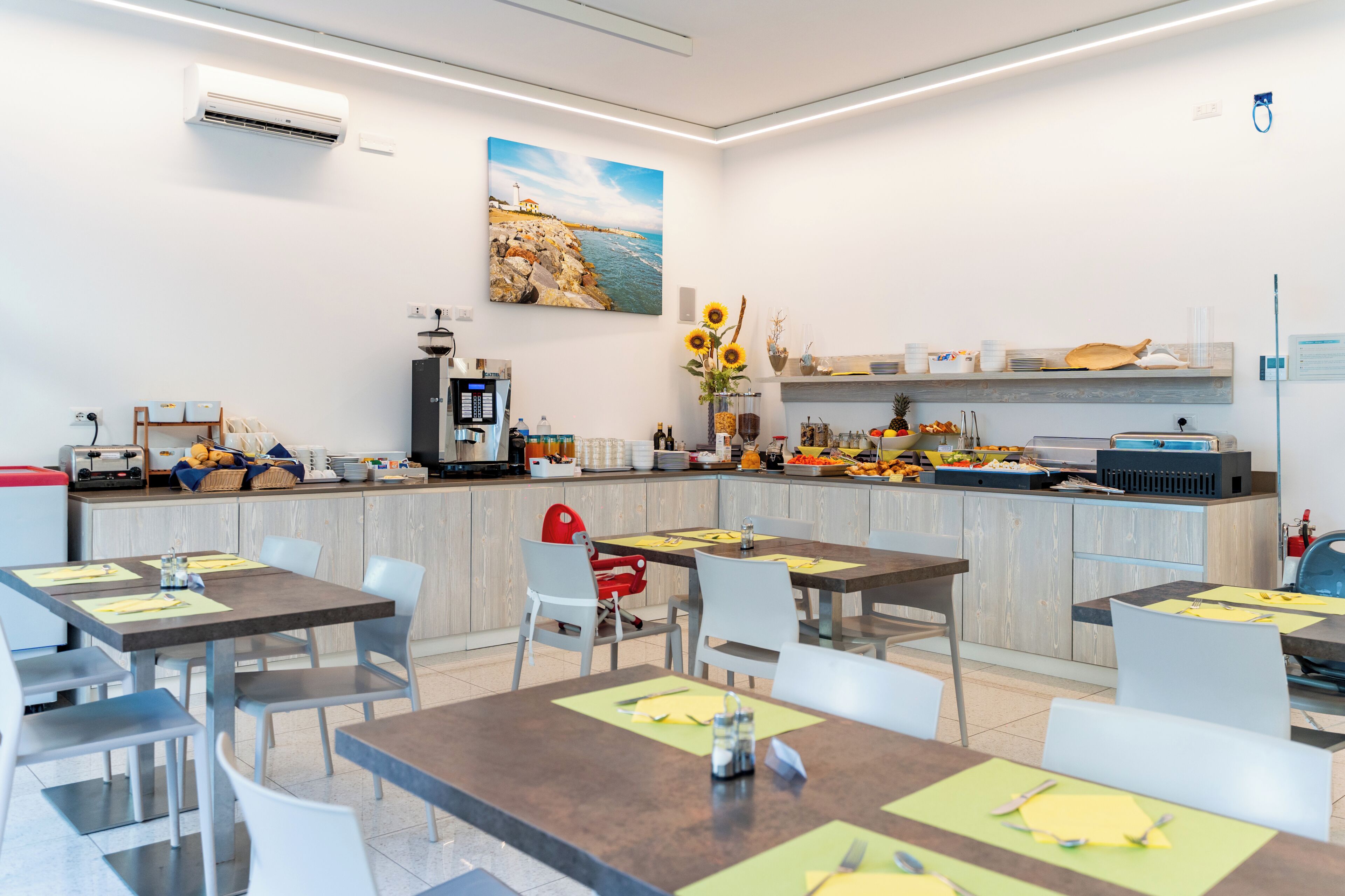 A modern dining area with tables and chairs, a coffee machine, and a buffet counter with various food items.