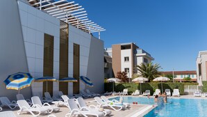 A poolside area with sun loungers and umbrellas, a clear blue pool, and modern buildings in the background. - Residenza Turistica Alberghiera Blue Marine (San Michele al Tagliamento)