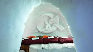An igloo with a bed inside, featuring a white blanket, a white pillow, and a red blanket.