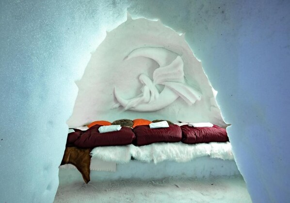 Een iglooe met een bed erin, voorzien van een witte deken, een wit kussen en een rode deken.