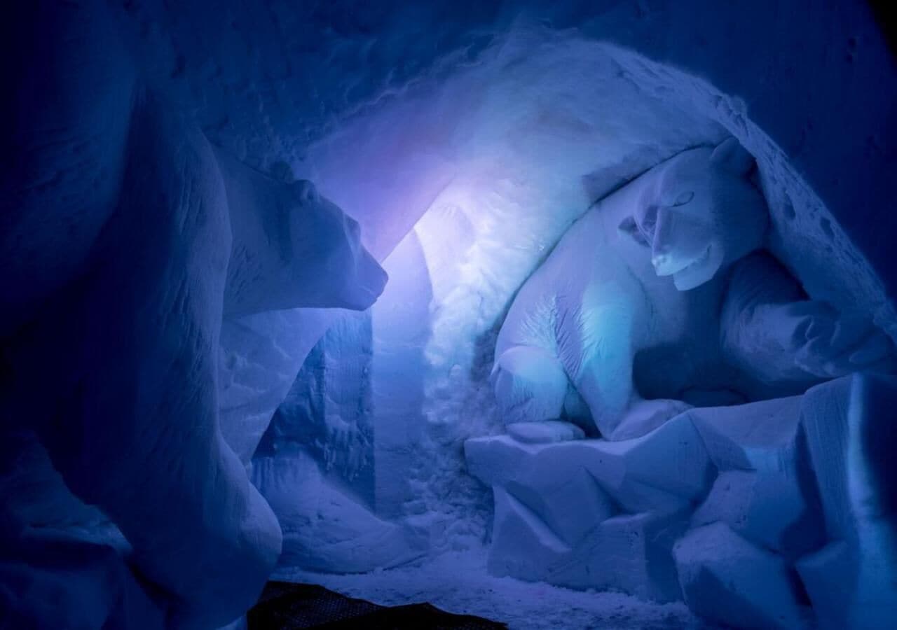 Une grotte de glace ornée d’une sculpture d’ours et éclairée par une source de lumière.