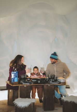 Une famille est assise autour d’une table en bois, avec un décor rustique en arrière-plan.