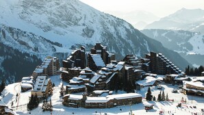 A snow-covered mountain resort with multiple buildings, ski slopes, and a ski lift.