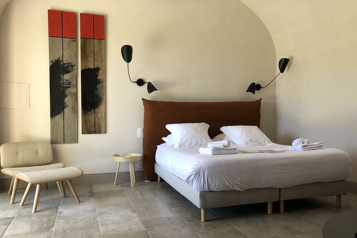 Quarto moderno com uma cama grande, uma mesinha de cabeceira, uma cadeira e uma mesa redonda.