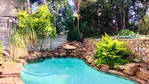A swimming pool with a stone wall and greenery around it. - Royaltics Place (Randburg)