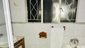 A bathroom with a toilet, sink, bathtub, and two windows. - Royaltics Place (Randburg)