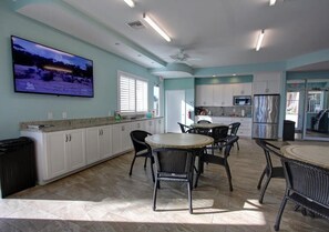 Una cocina amplia con armarios blancos, una isla grande con sillas, un televisor de pantalla plana y un ventilador de techo.