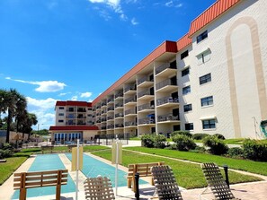 Hotel features a multi-story structure with balconies on each floor, a swimming pool and lounge chairs surrounded by lush greenery.