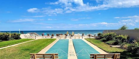 Un espace extérieur ensoleillé comprenant un terrain de jeu de shuffleboard, des bancs et une vue sur l’océan.