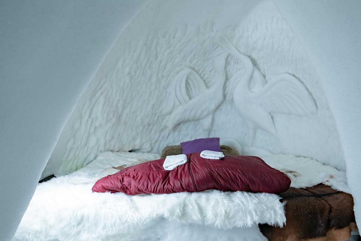 Una habitación acogedora con una cama que tiene una colcha blanca y mullida, y una almohada roja.
