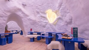 Interior de un hotel de hielo con mesas y bancos azules, una ventana de hielo con forma de corazón y un letrero.