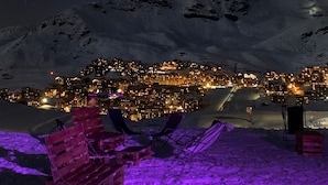 Paisaje nevado de montañas de noche con un pueblo iluminado al fondo.