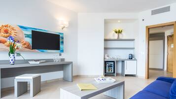 Una sala de estar moderna con televisor de pantalla plana, una mesa de centro, un sofá azul y una cocina con refrigerador y microondas.