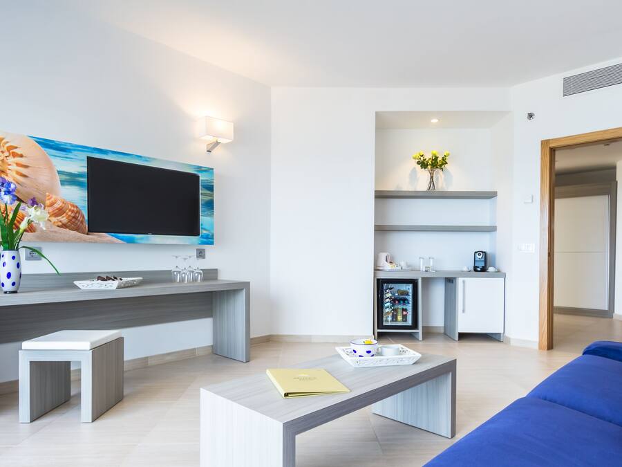 Una sala de estar moderna con televisor de pantalla plana, una mesa de centro, un sofá azul y una cocina con refrigerador y microondas.