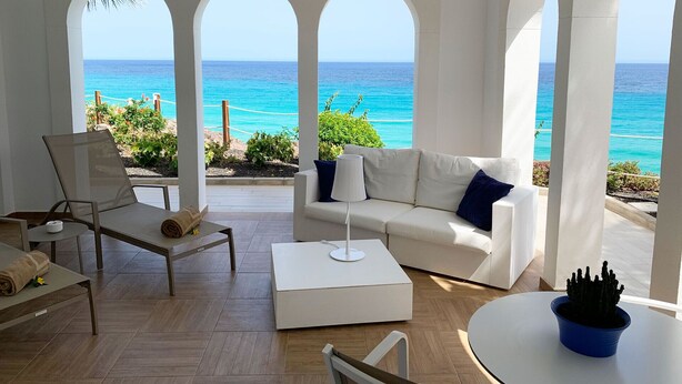 A sunlit room with a white sofa, a chair, and a table, overlooking a turquoise sea through arched windows. - Royal Palm Resort & Spa - Adults Only (Pajara)
